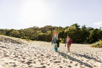 Full length of mother and daughter walking on sand at beach against sky during sunset