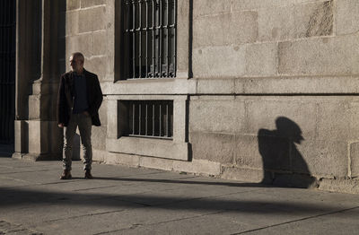 Adult man in suit standing on street against wall with sunlight and shadow