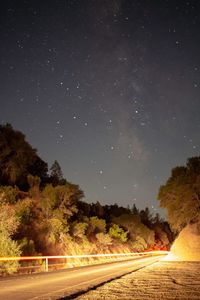 Empty road amidst trees against sky at night