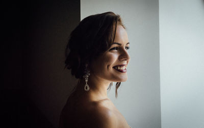 Close-up of thoughtful young woman smiling against wall