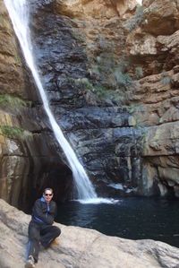 Man sitting on rock by waterfall