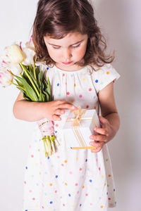 Cute girl holding gift box while holding flowers