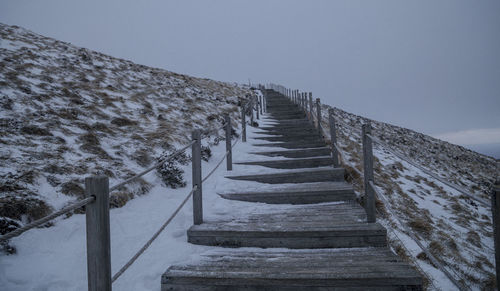 Empty footpath amidst snow against clear sky