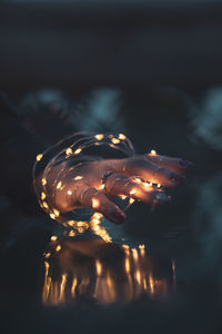 Cropped hand of woman with illuminated string lights at night