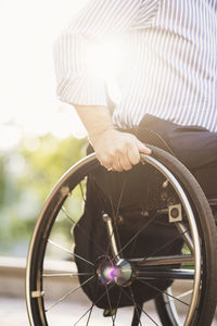 Midsection of man sitting in wheelchair on sunny day outdoors