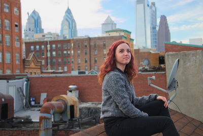 Young woman sitting on roof in city