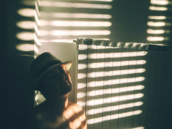 Portrait of young woman with hat at home against a white wall with beautiful shadows in sunset time