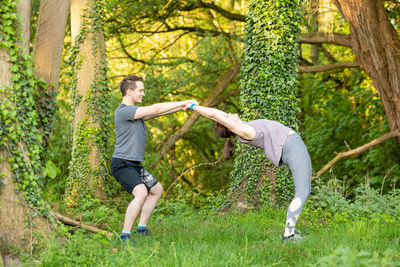 Side view of man assisting woman in doing yoga on land