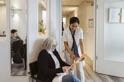 Smiling female healthcare worker standing by senior patient looking at clipboard in clinic