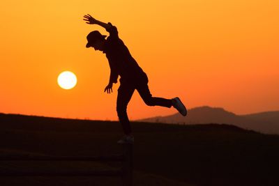 Silhouette man jumping on field against orange sky