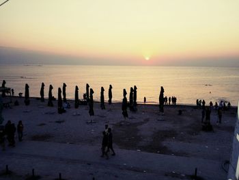 Silhouette people on beach against sky during sunset