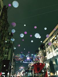 Low angle view of illuminated ferris wheel against buildings in city