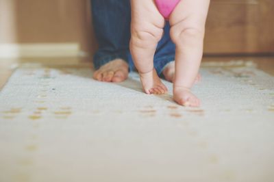 Low section of parent with baby on carpet at home