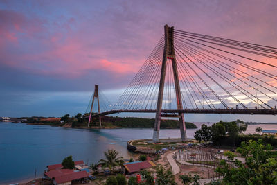 View of suspension bridge over river against cloudy sky