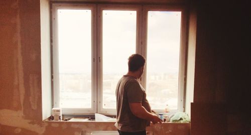 Side view of man looking through window at home