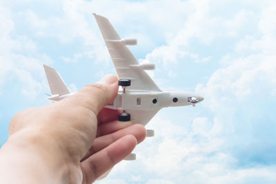 Close-up of hand holding toy airplane against sky