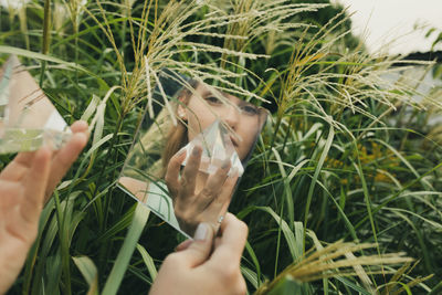 Reflection of woman holding prism in mirror against plants