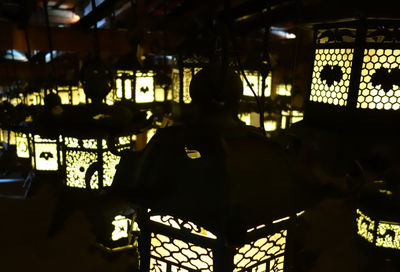 Rear view of silhouette man sitting in illuminated amusement park at night