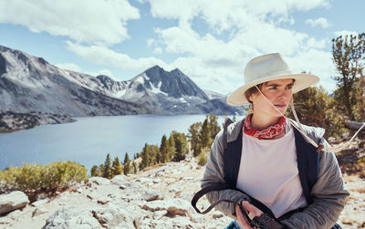 Middle aged female in hat holding camera by lake in mountains