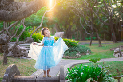 Cute girl wearing blue dress standing against trees in park