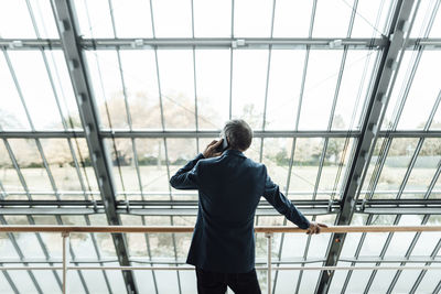 Businessman talking on mobile phone while standing at railing in corridor