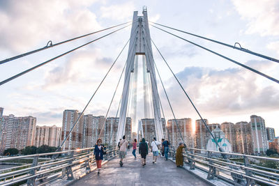 People on suspension bridge against cloudy sky