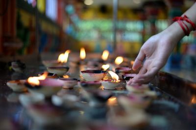 Close-up of hand burning candles in temple against building