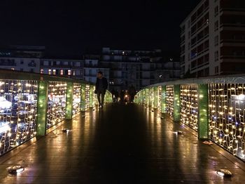 Rear view of man walking on illuminated bridge at night