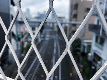 Close-up of metal fence against bridge in city