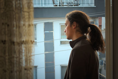 Side view of man standing by window at home