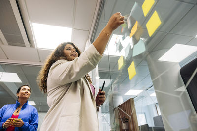 Low angle view of female entrepreneur standing near colleague while doing brainstorming at office