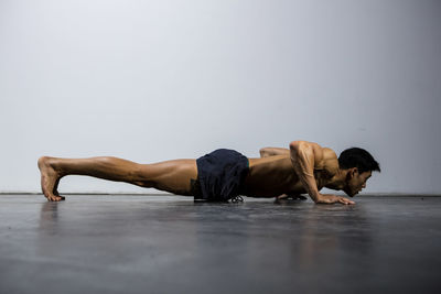 Shirtless man doing push-ups against wall