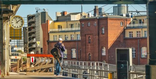 Rear view of man with guitar standing at railroad station