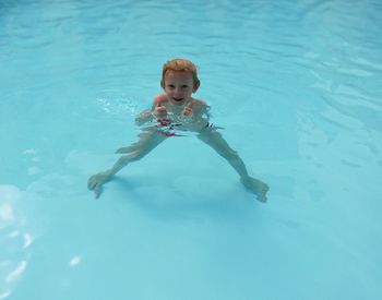 High angle portrait of shirtless boy showing thumbs up while swimming in pool