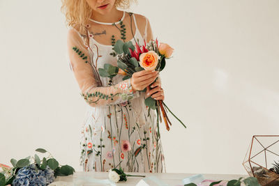 Midsection of woman holding flower standing against white background