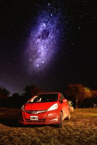 Red car on field against sky at night