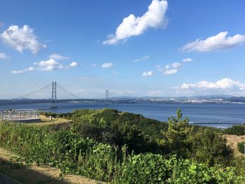 View of suspension bridge over sea against cloudy sky