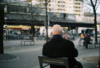 Rear view of man sitting on bench in city