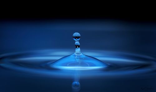 Close-up of drop falling on water against black background