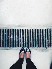 Low section of woman standing by drain on footpath