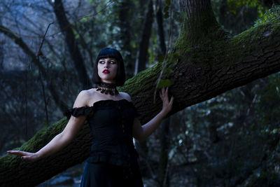 Portrait of woman standing by tree trunk in forest