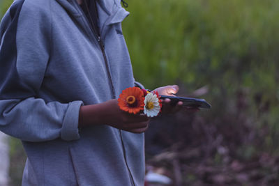 Midsection of woman holding flowers using smart phone while standing outdoors