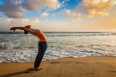 Rear view of woman standing at beach against sky during sunset