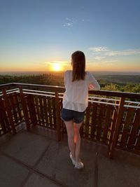 Rear view of woman standing  against sky during sunset