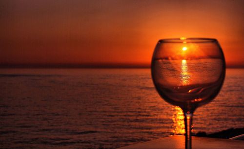 Close-up of beer glass against sea during sunset