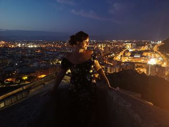 Woman standing by illuminated buildings in city at night