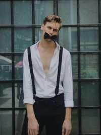 Portrait of young man with bow tie on mouth standing against glass