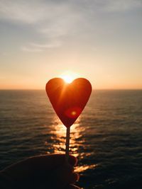 Hand holding heart shape candy against sky during sunset