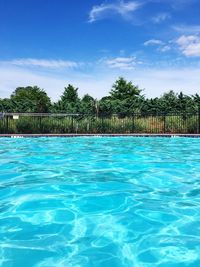 Swimming pool by trees against blue sky