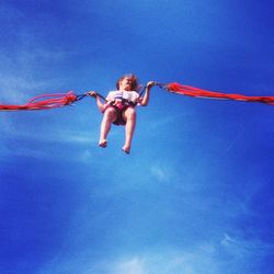 Low angle view of girl jumping against blue sky